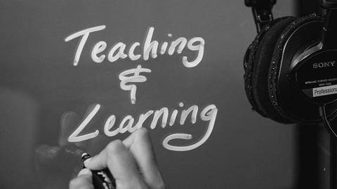 a hand writing Teaching & Learning on a glass board - photo Casey Smerczynski